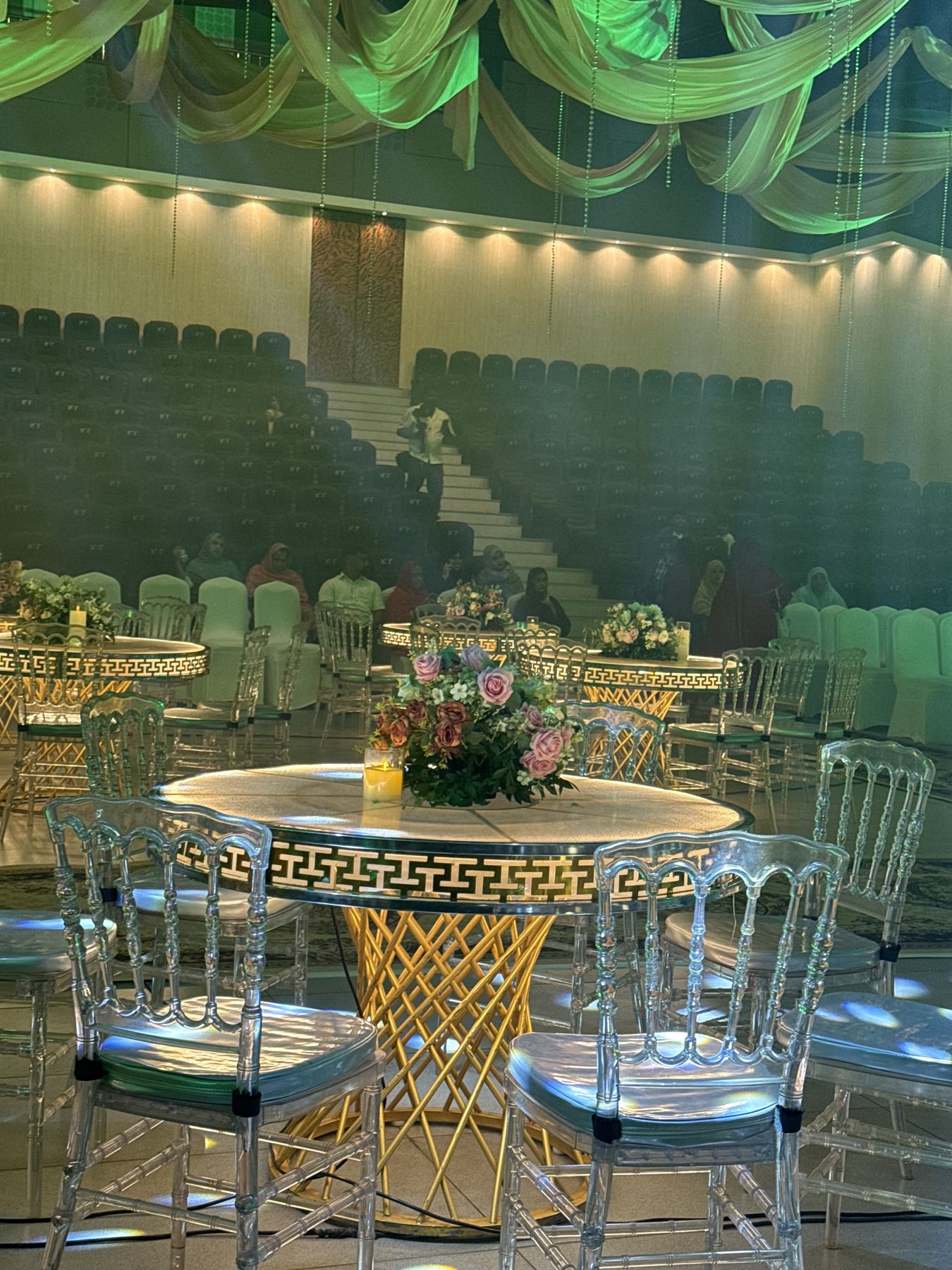 Gold lattice table with florals and clear chairs under green light