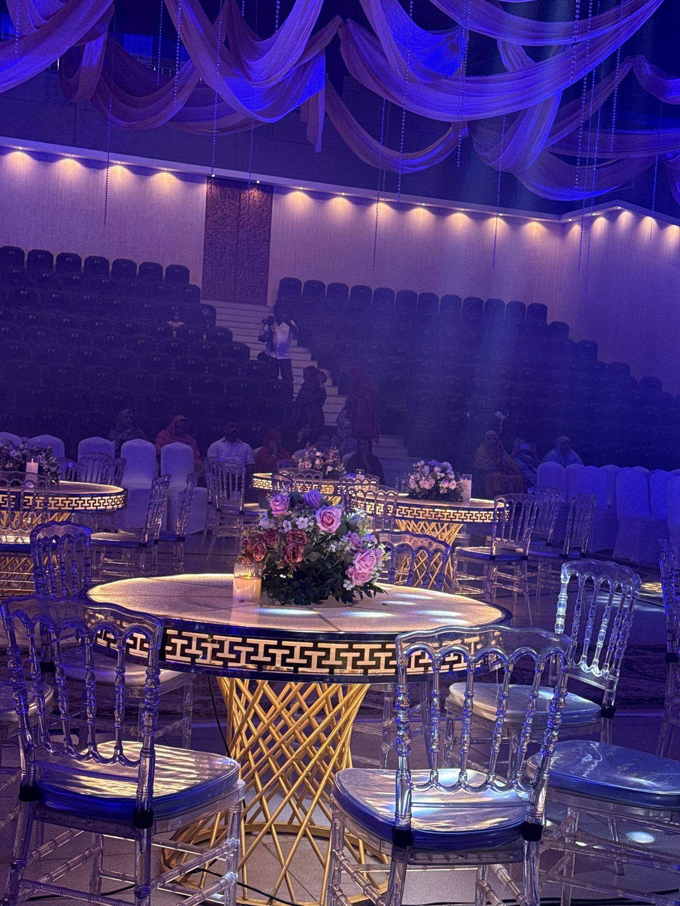 Banquet table with gold lattice base and floral centrepiece under violet lighting
